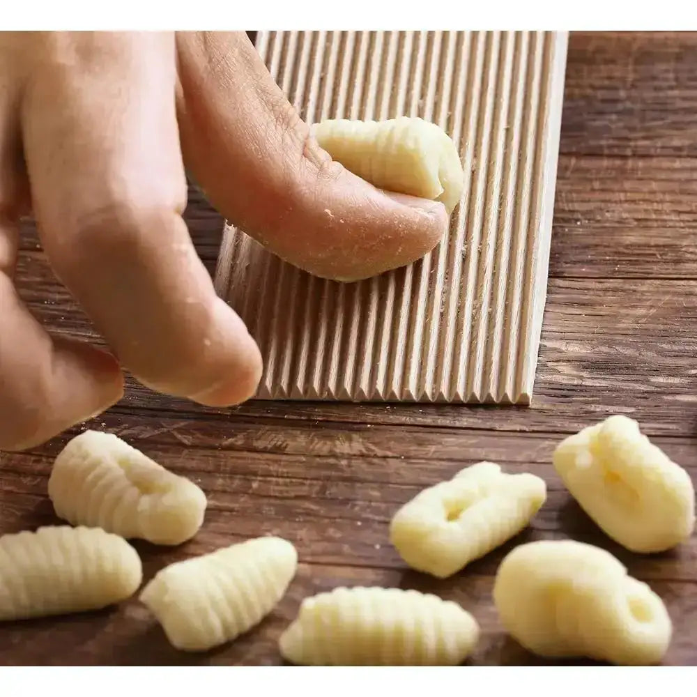 Hand forming gnocchi on a wooden surface with a pasta machine in the background.