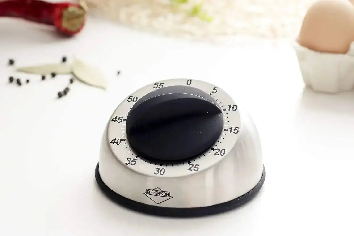 Kitchen timer on a white surface with ingredients in the background