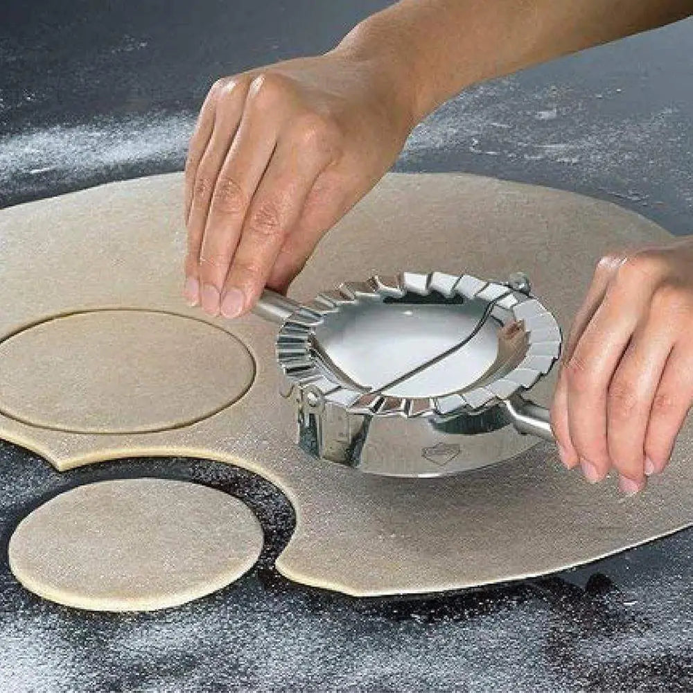 Person using a ravioli stamp on rolled-out dough on a dark surface.
