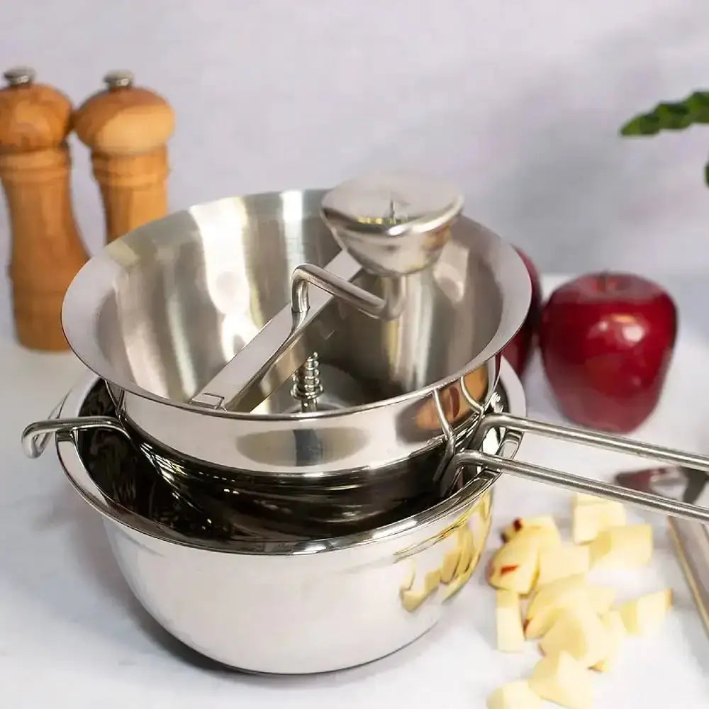 Set of stainless steel measuring cups on a kitchen counter with apples and spices in the background.