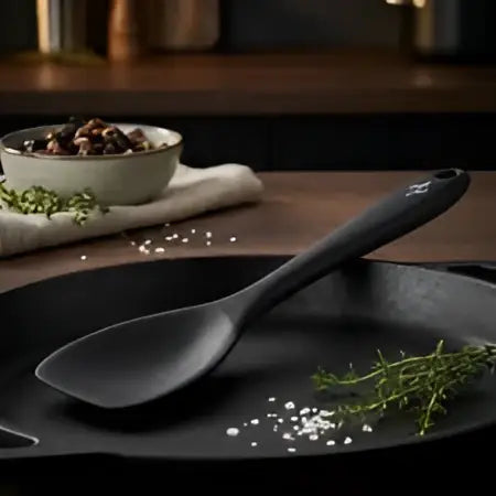 Black spoon on a black plate with herbs and spices on a wooden surface