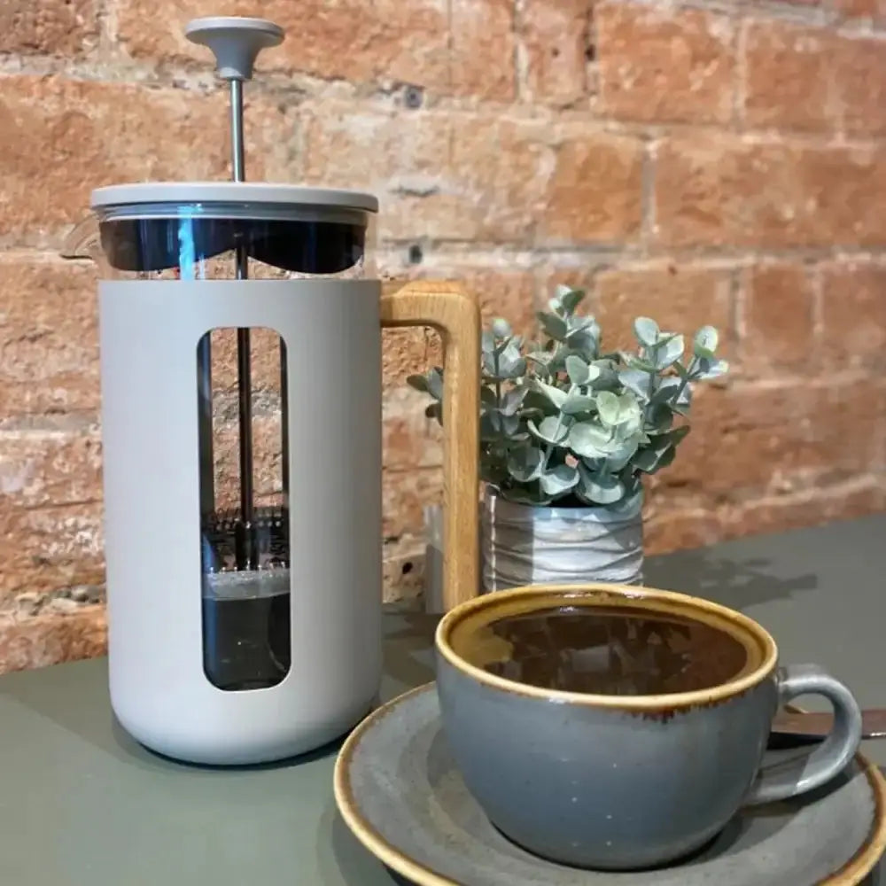 French press coffee maker with a cup of coffee on a table against a brick wall.