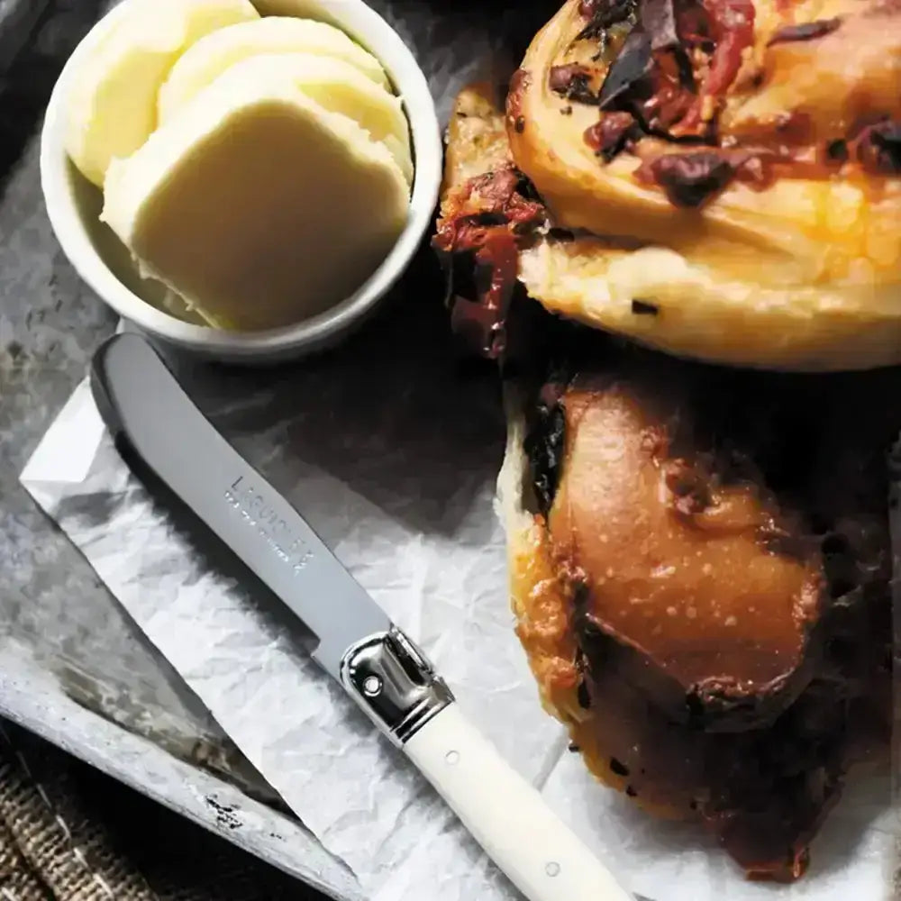 Baked goods with a knife and bowl of butter on a rustic surface
