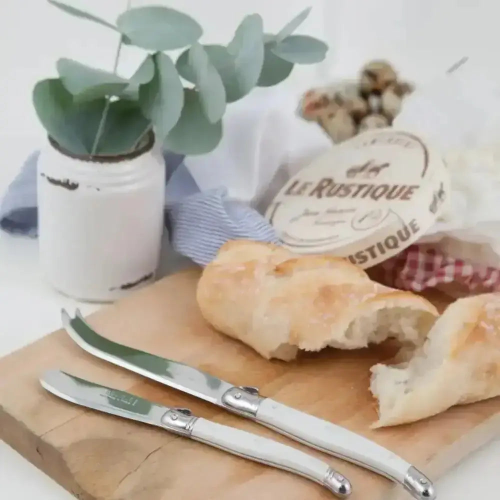 Bread on a wooden board with cheese knives and a plant in the background