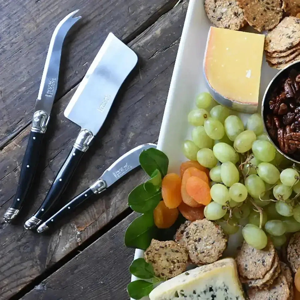 Assorted cheeses, crackers, and fruits with cheese knives on a wooden surface