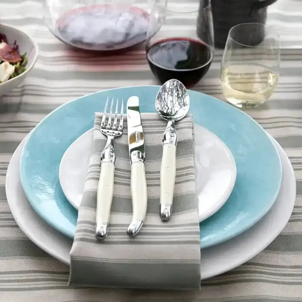 Dining table setting with blue plates, silverware, and a striped cloth.