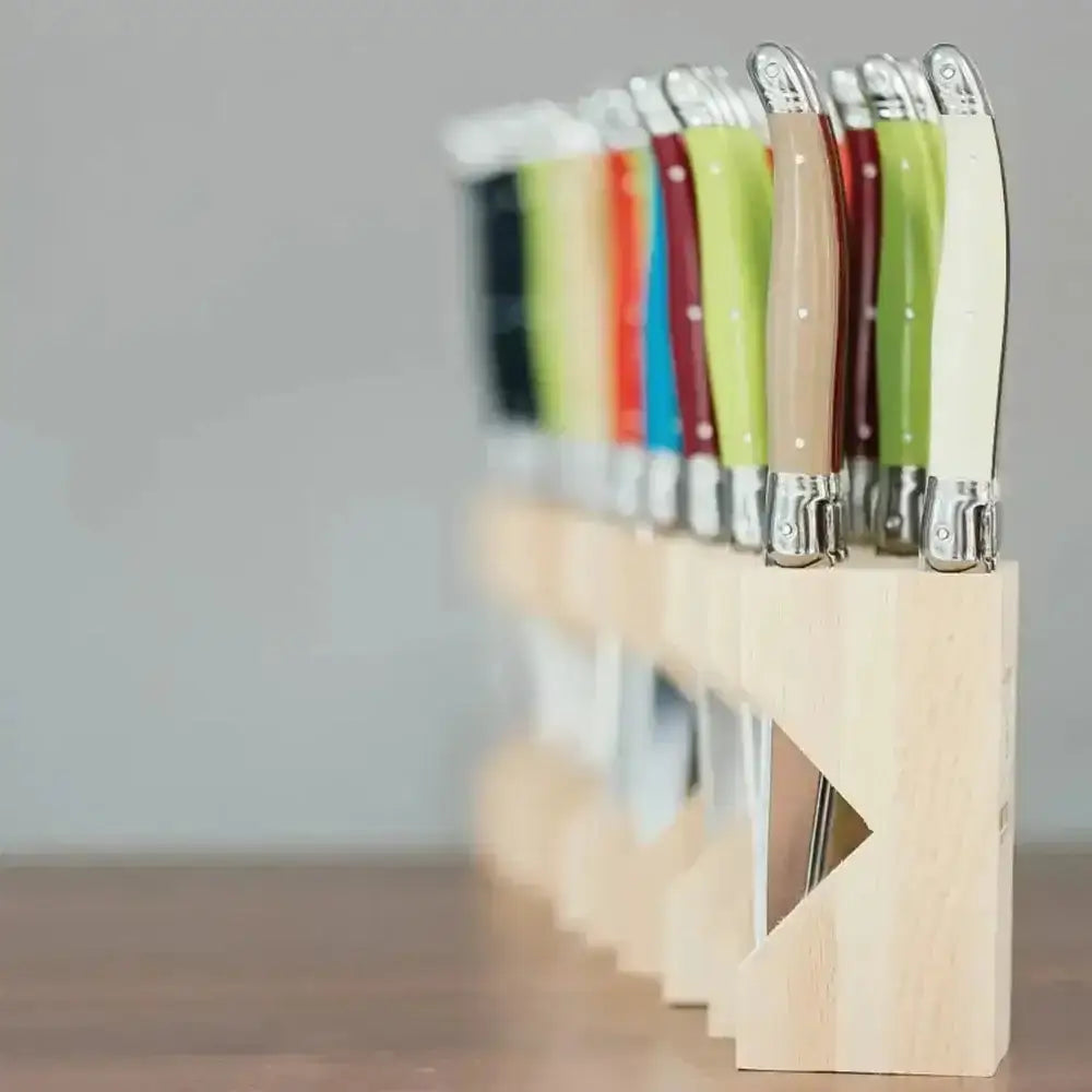 Set of colorful knives with wooden handles in a holder on a neutral background