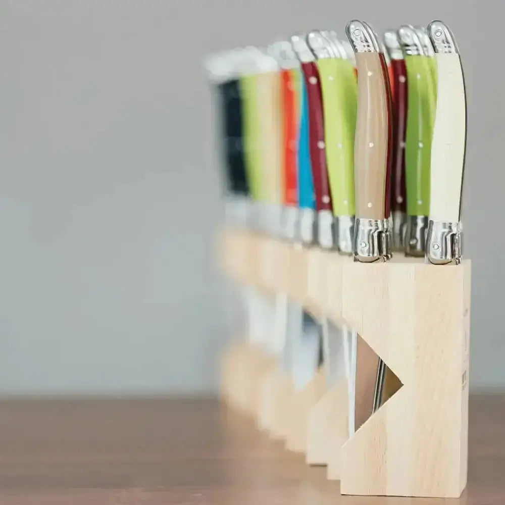 Set of colorful knives in a wooden holder on a neutral background