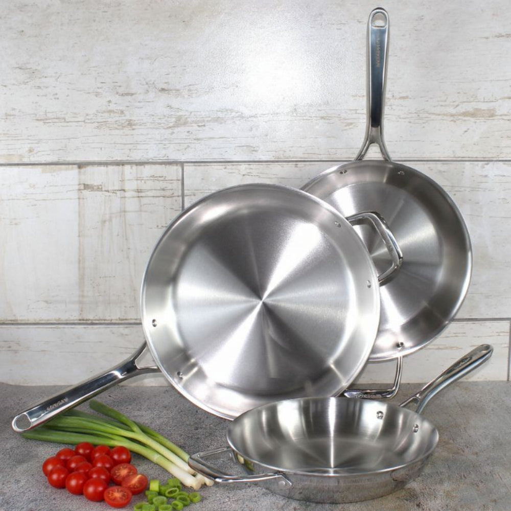 Set of stainless steel cookware on a kitchen counter with vegetables.
