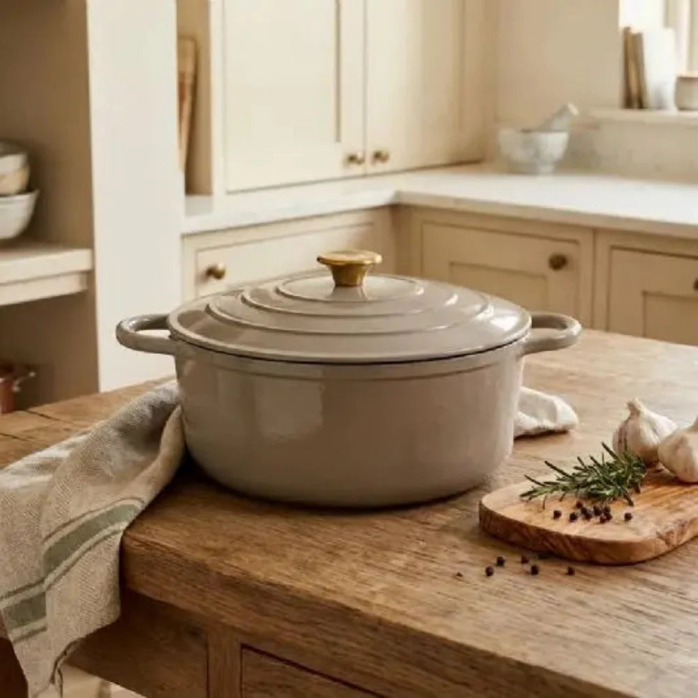 Beige enameled cast iron Dutch oven on a wooden kitchen counter with a neutral color scheme.