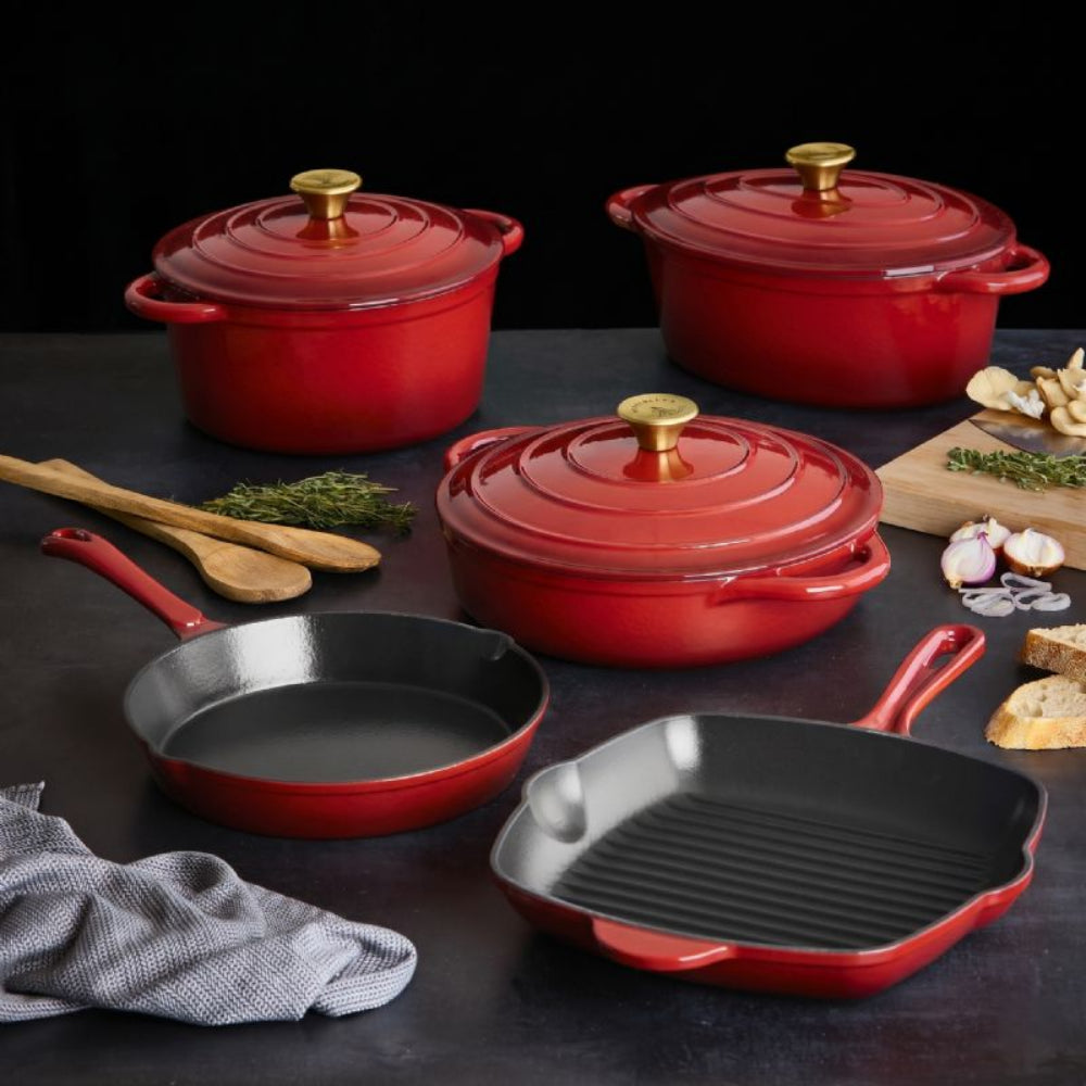 Set of red cookware including pots and pans on a dark surface with ingredients.