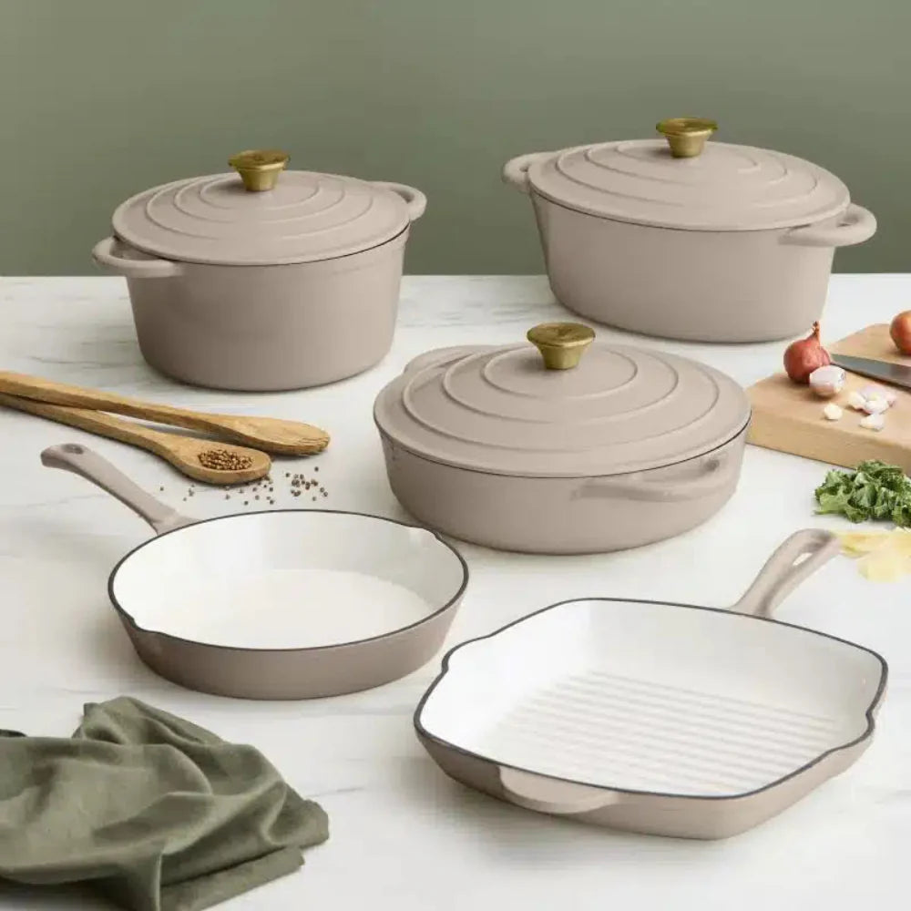 Set of beige cookware including pots and pans on a light surface with a green background