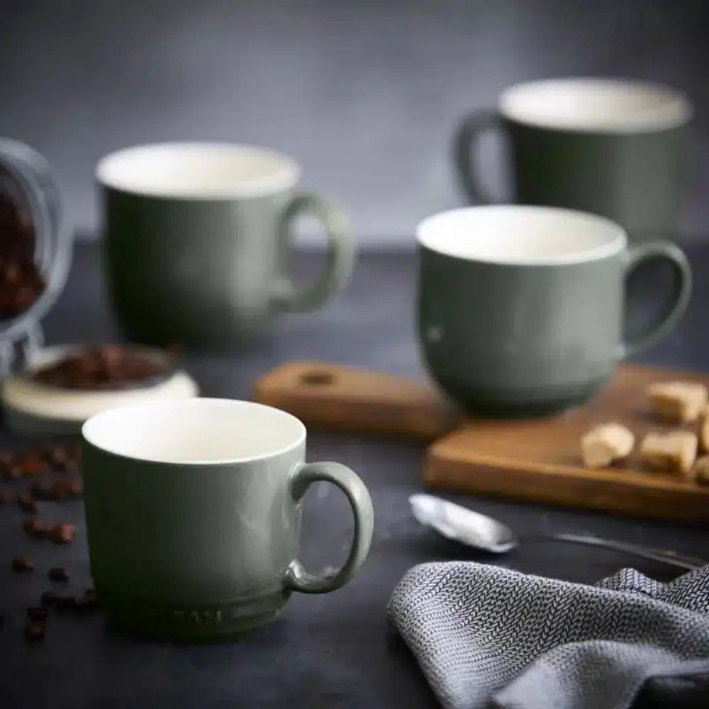 Set of green mugs on a dark surface with coffee beans and sugar cubes.