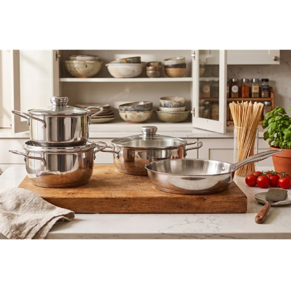 Set of stainless steel cookware on a wooden cutting board in a kitchen.