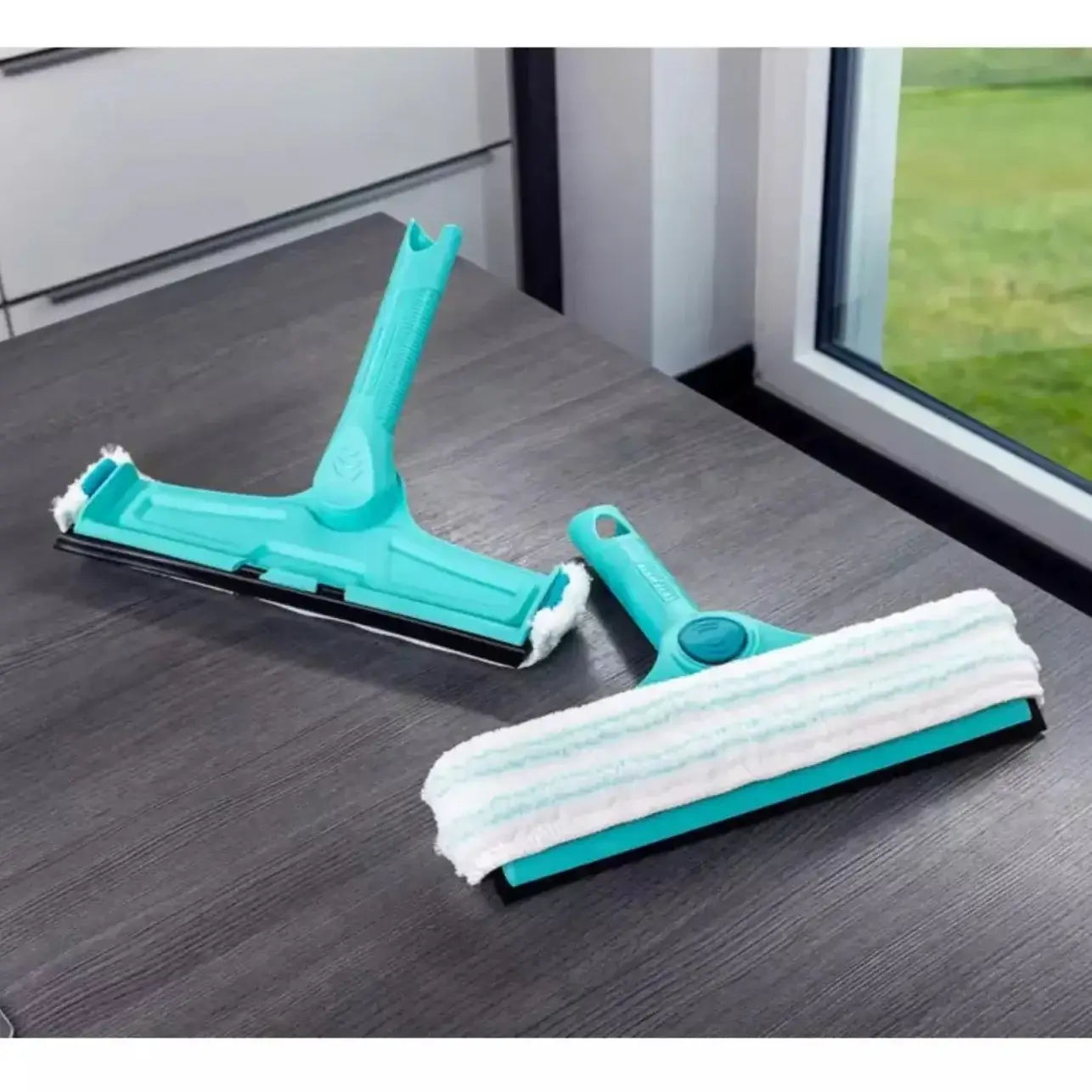 Two cleaning tools on a wooden surface with a window in the background