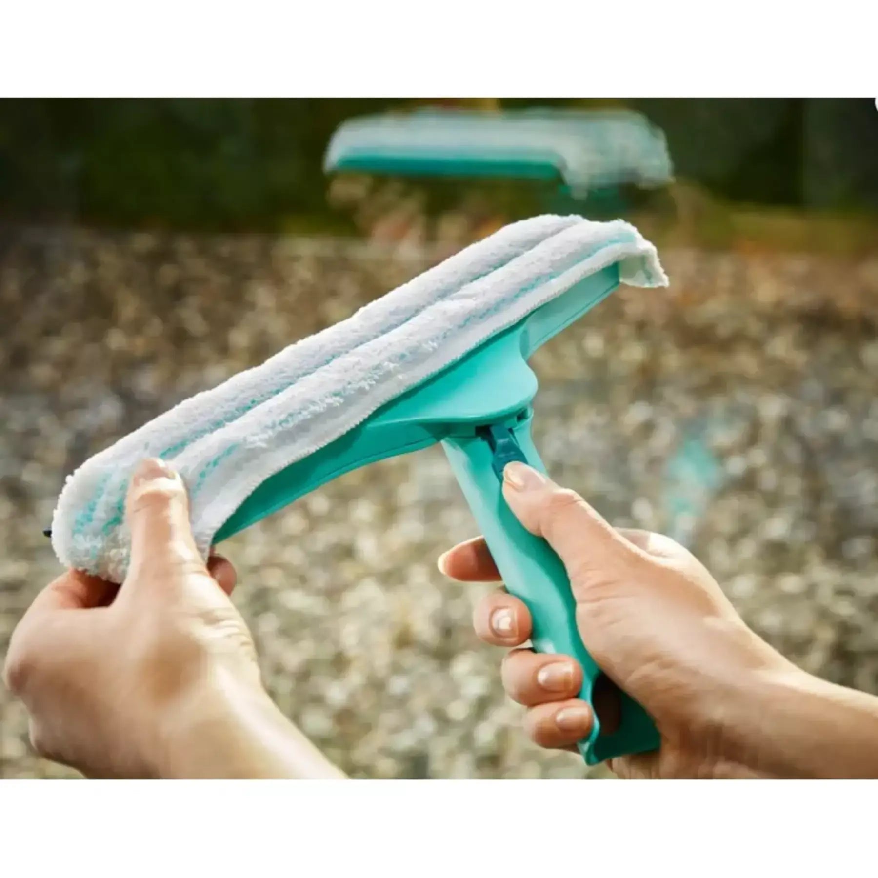 Turquoise window cleaning tool with a white cloth being used outdoors.