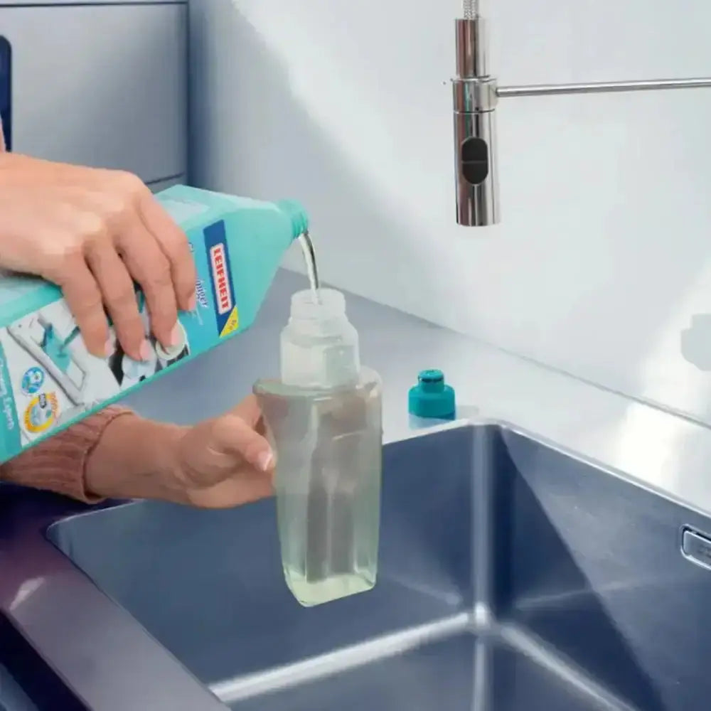 Person pouring liquid from a bottle into a spray bottle in a kitchen sink.