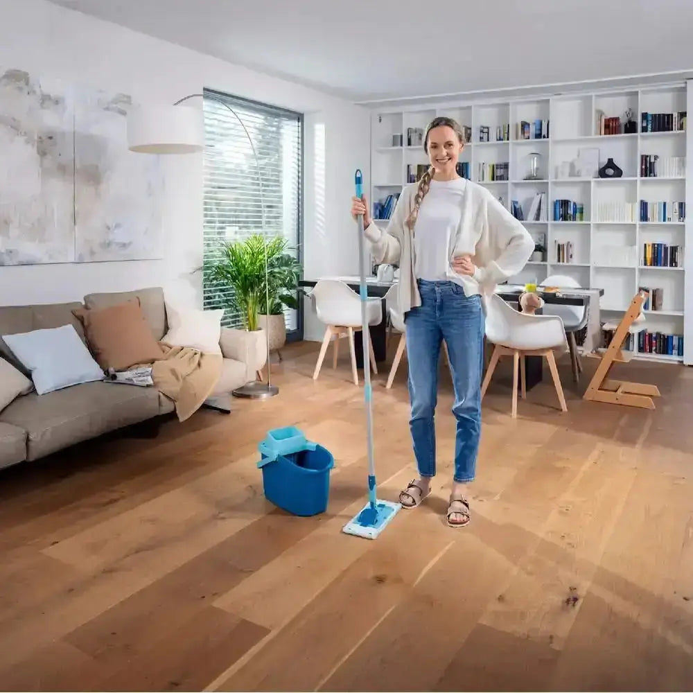 Woman holding a cleaning mop in a living room with wooden floor and bookshelves.