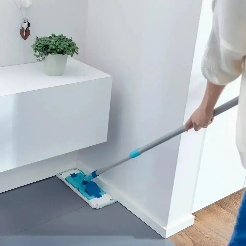 Person cleaning a floor with a mop in a room with white walls and a plant on a shelf.