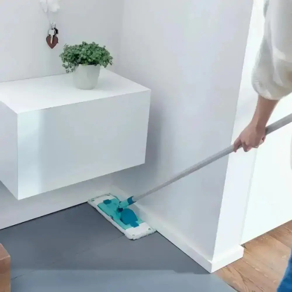 Person using a cleaning tool under a white cabinet with a plant on top.