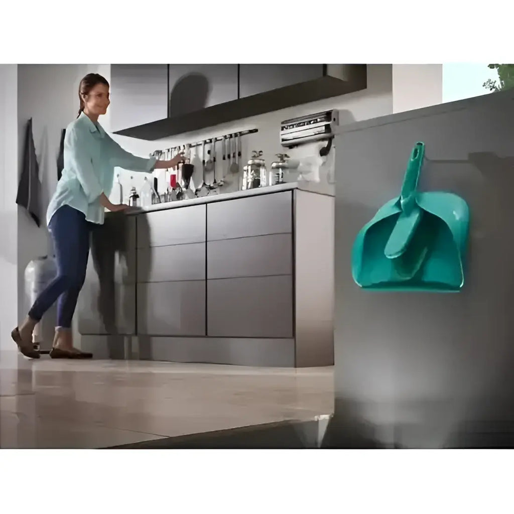 Woman in a kitchen with a teal dustpan and brush set on a refrigerator.