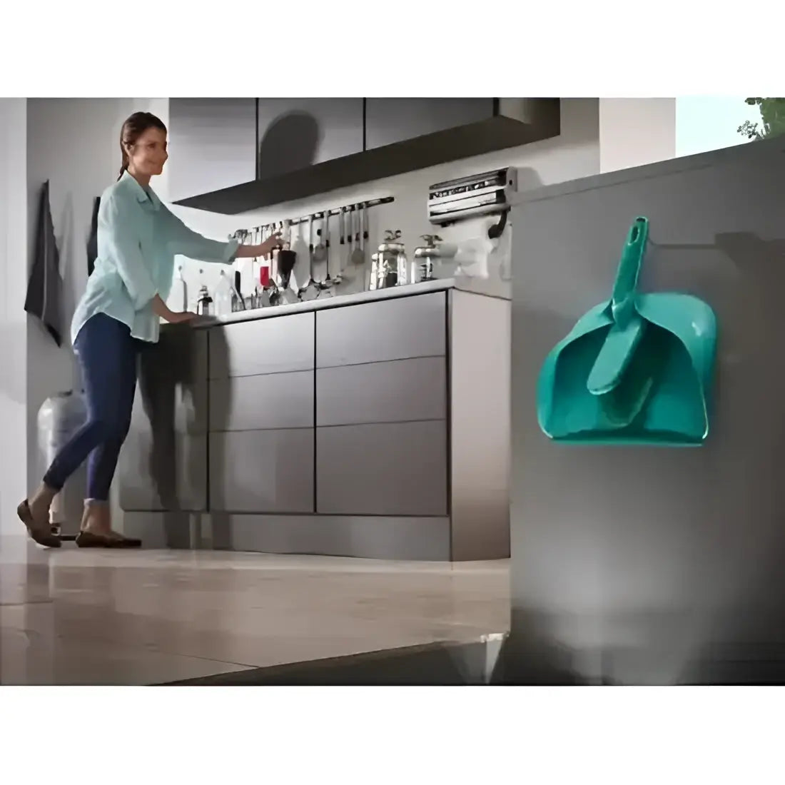 Woman in a kitchen with a teal dustpan and brush set on a refrigerator.