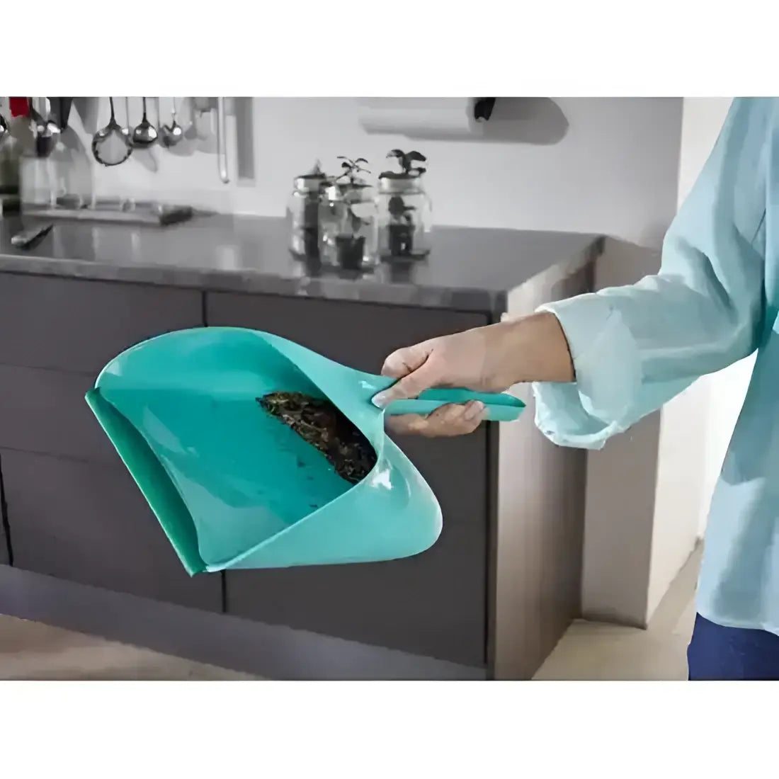 Person using a teal dustpan in a kitchen setting