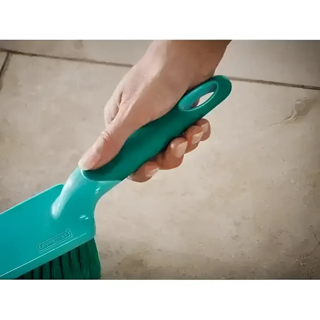 Teal brush with handle held by a hand on a tiled floor