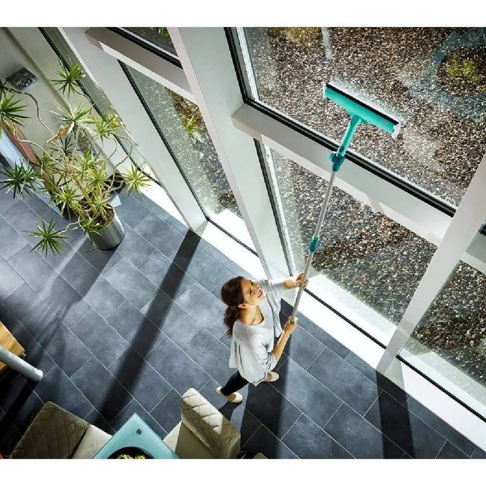 Person cleaning a large window with a squeegee in a modern indoor setting.