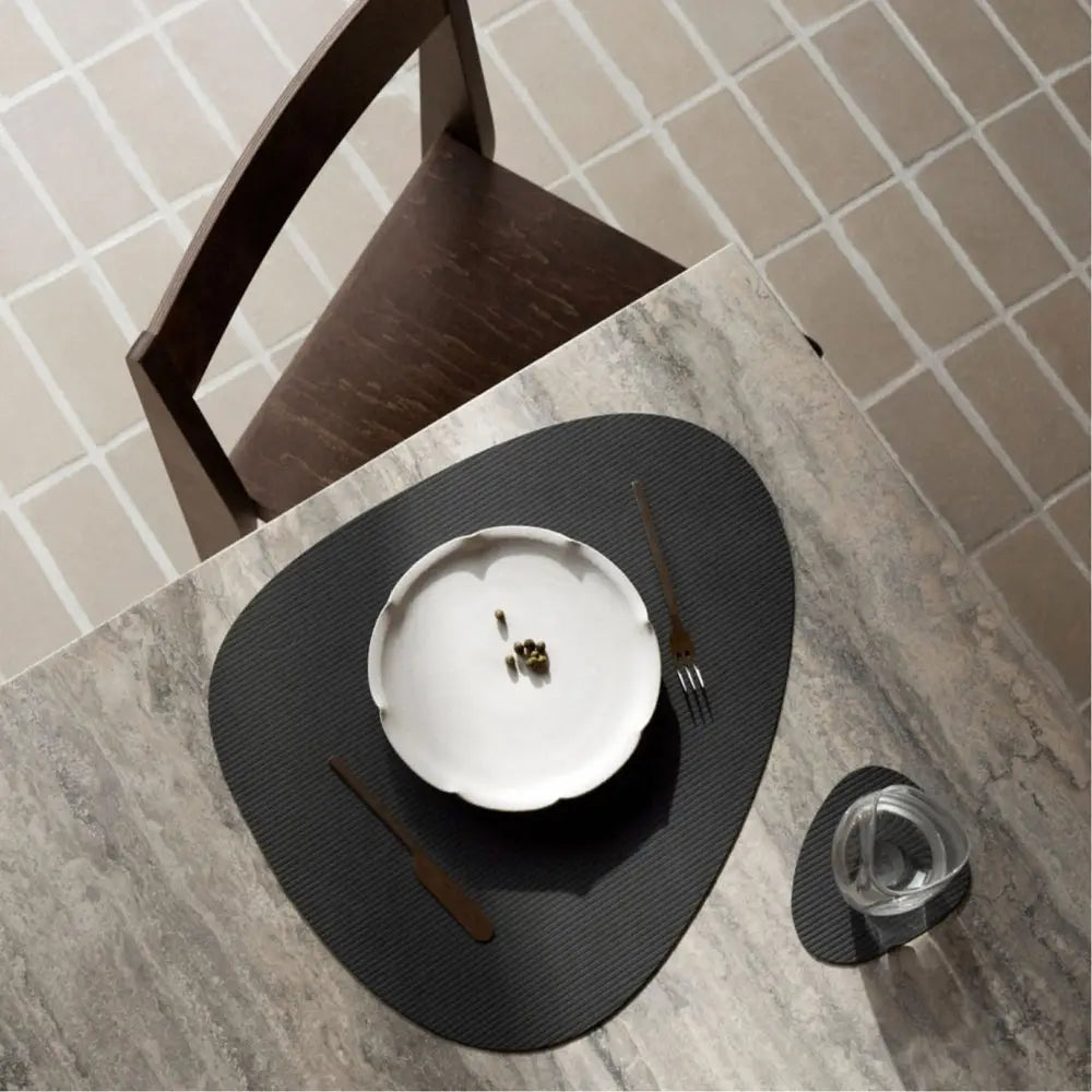Dining table setting with a white plate, black cutlery, and glass on a gray surface.