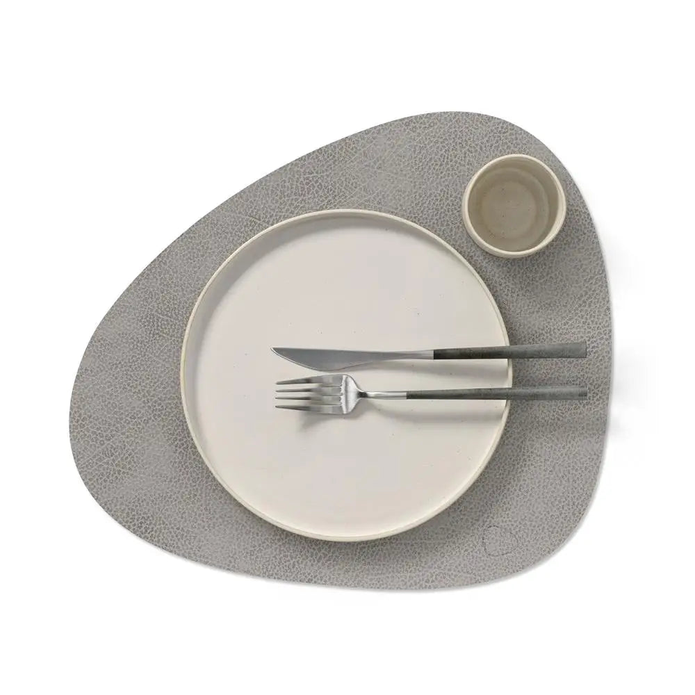 Dinner setting with a plate, knife, fork, and cup on a textured gray placemat.