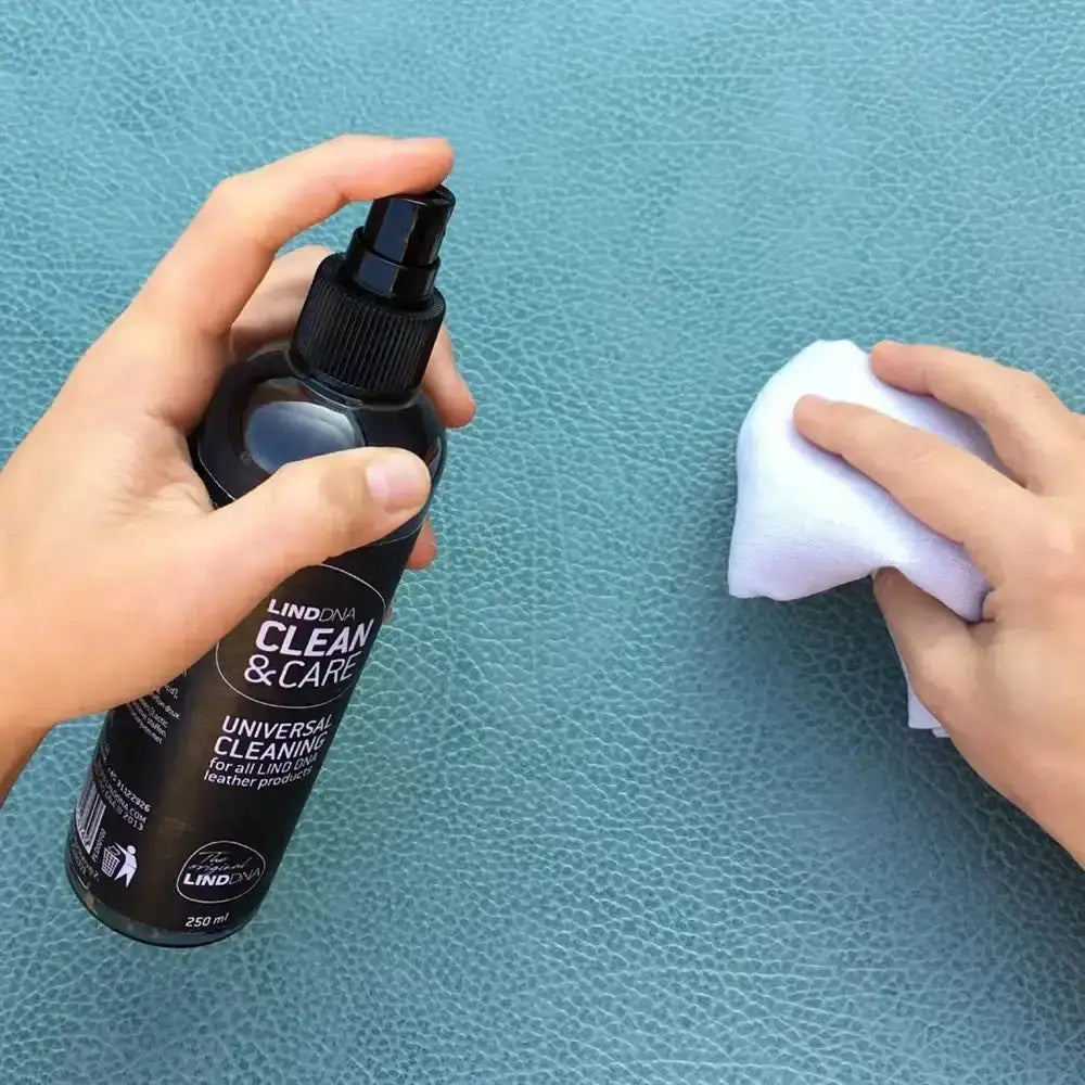 Person using a spray bottle labeled 'Clean & Care' on a textured blue surface.