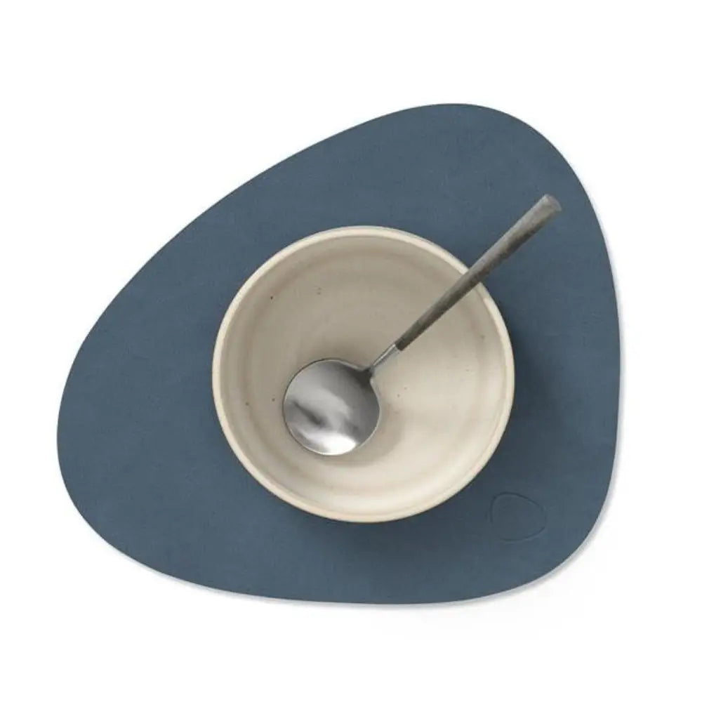 Blue placemat with a white bowl and silver spoon on a white background