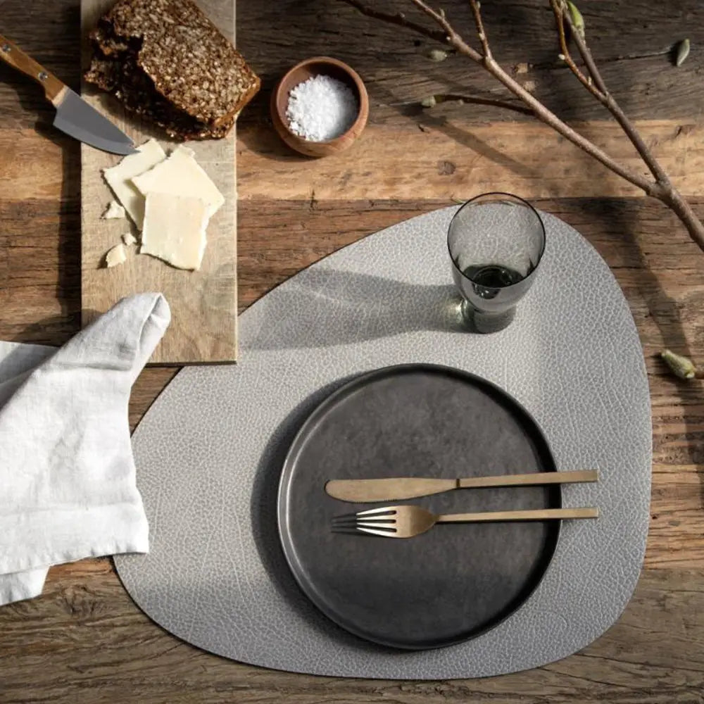 Dining table setting with gray plates, cutlery, and a wooden cutting board on a rustic wooden surface.