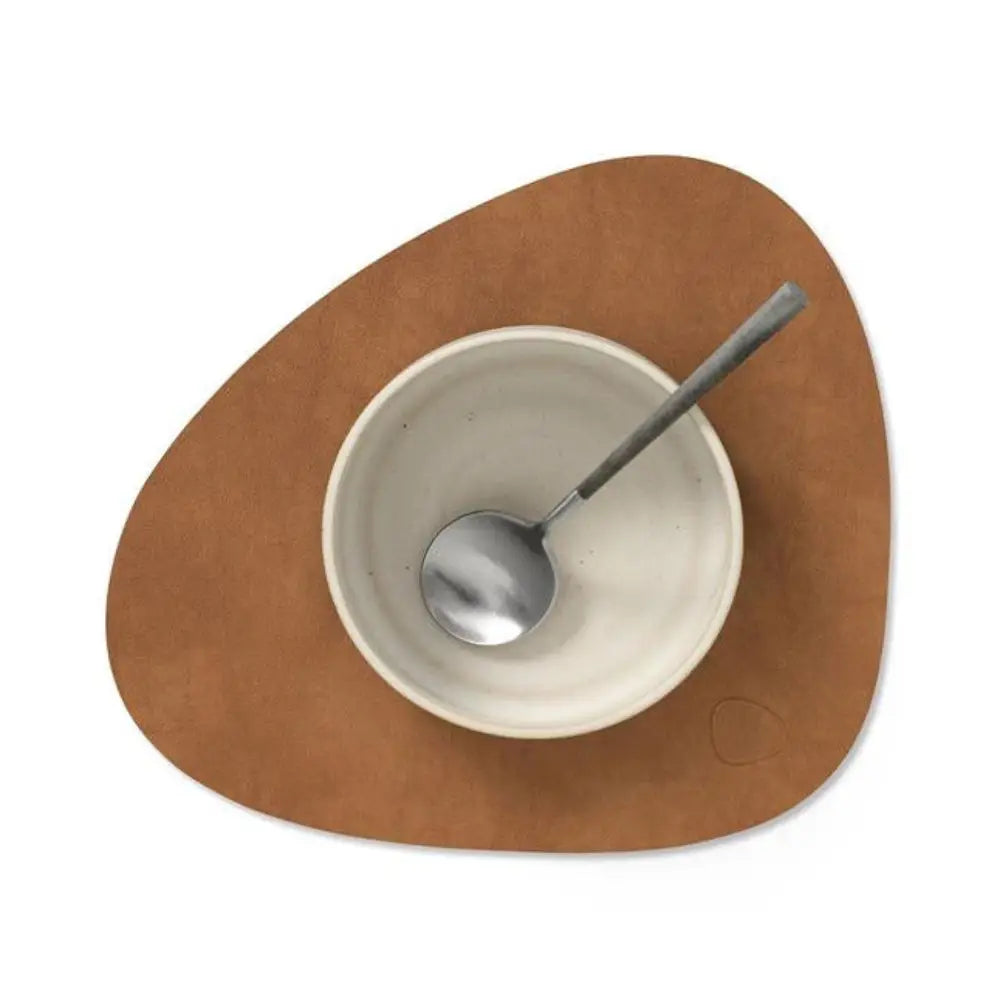 Brown placemat with a white bowl and silver spoon on a white background