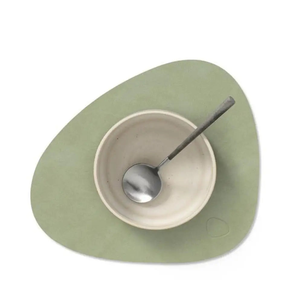 Green placemat with a white bowl and silver spoon on a white background