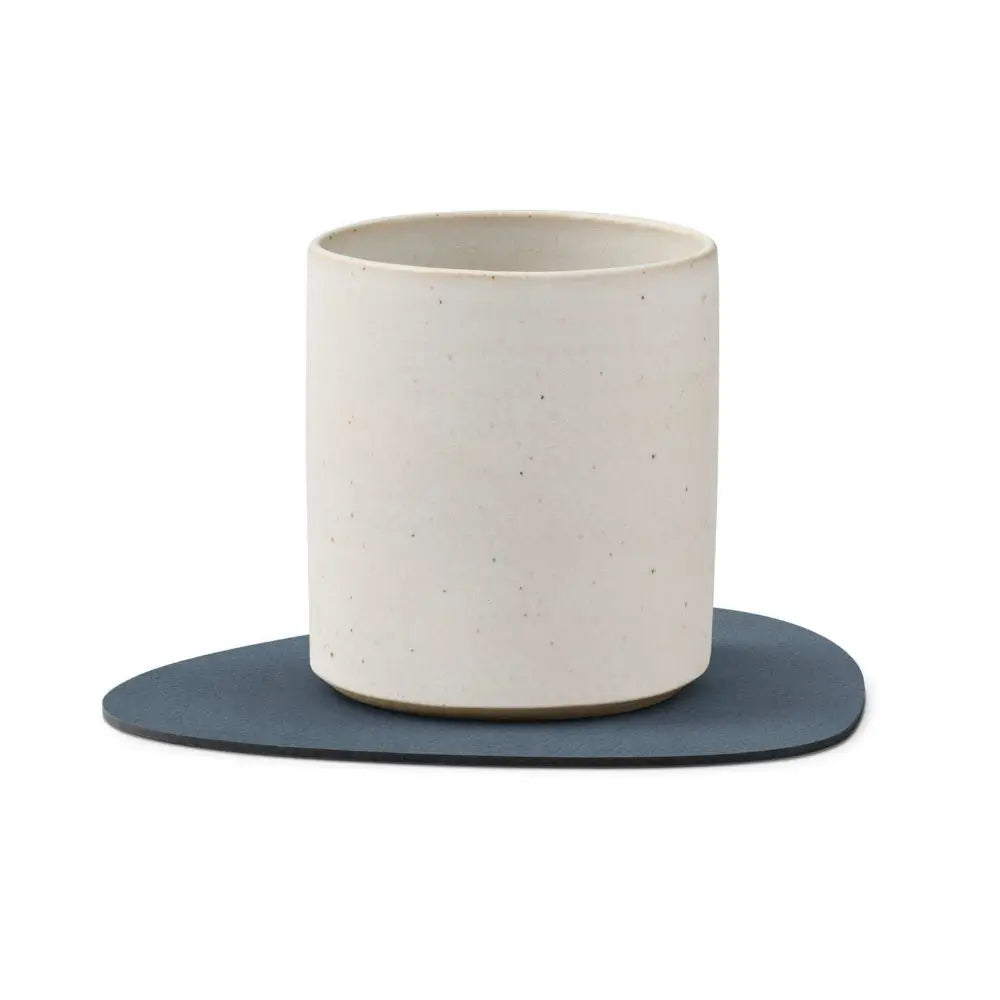 White ceramic cup with a blue coaster on a white background