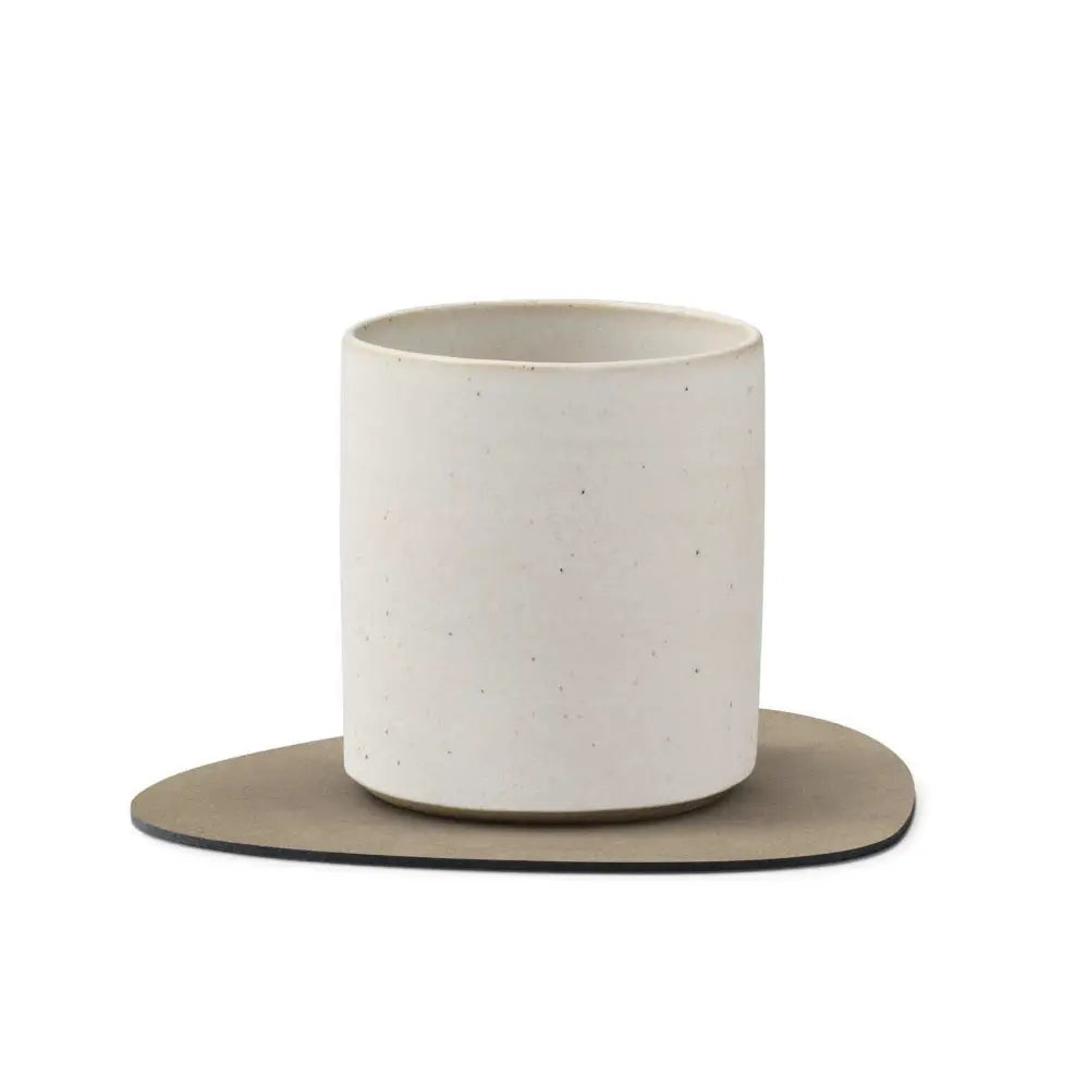 White ceramic cup on a leather coaster on a white background