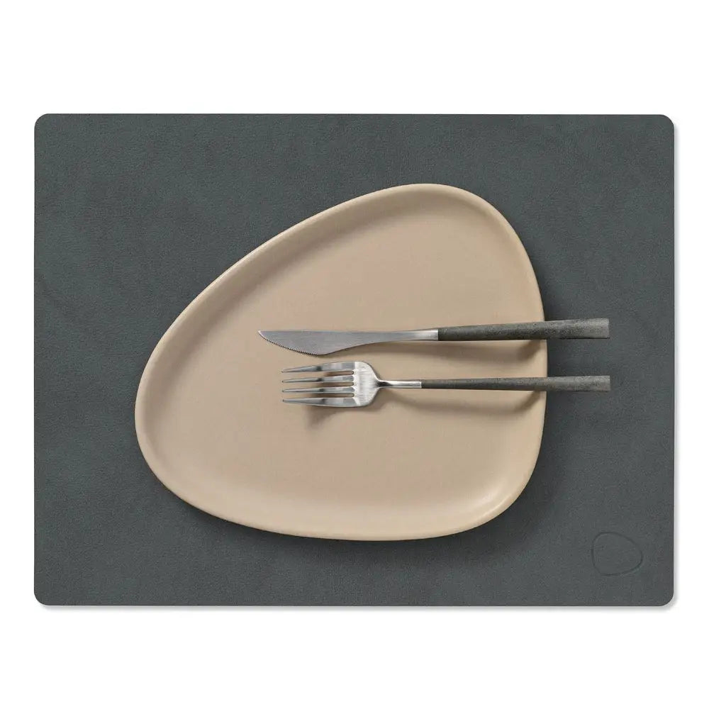 Beige plate with silverware on a dark gray placemat