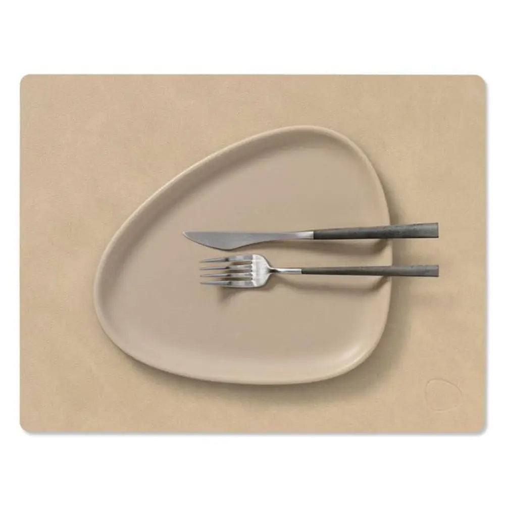 Beige ceramic plate with cutlery on a matching placemat against a white background