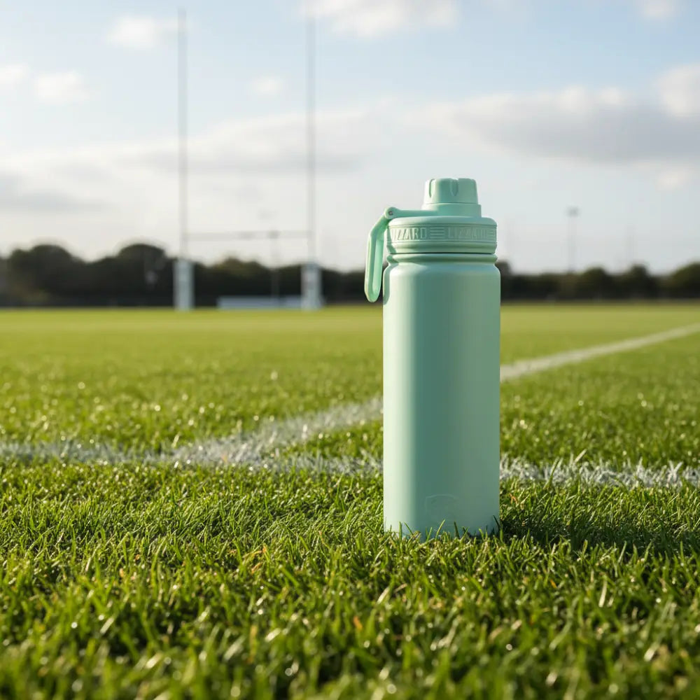 Sage water bottle on a grassy field with sports equipment in the background