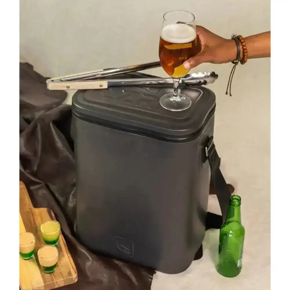 Black cooler bag with a glass of beer on top, surrounded by bottles and glasses.