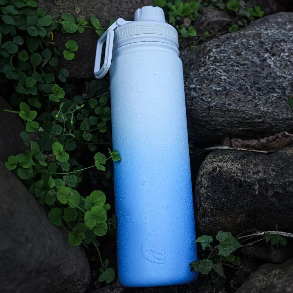 Blue water bottle with a white cap on a natural background of rocks and greenery