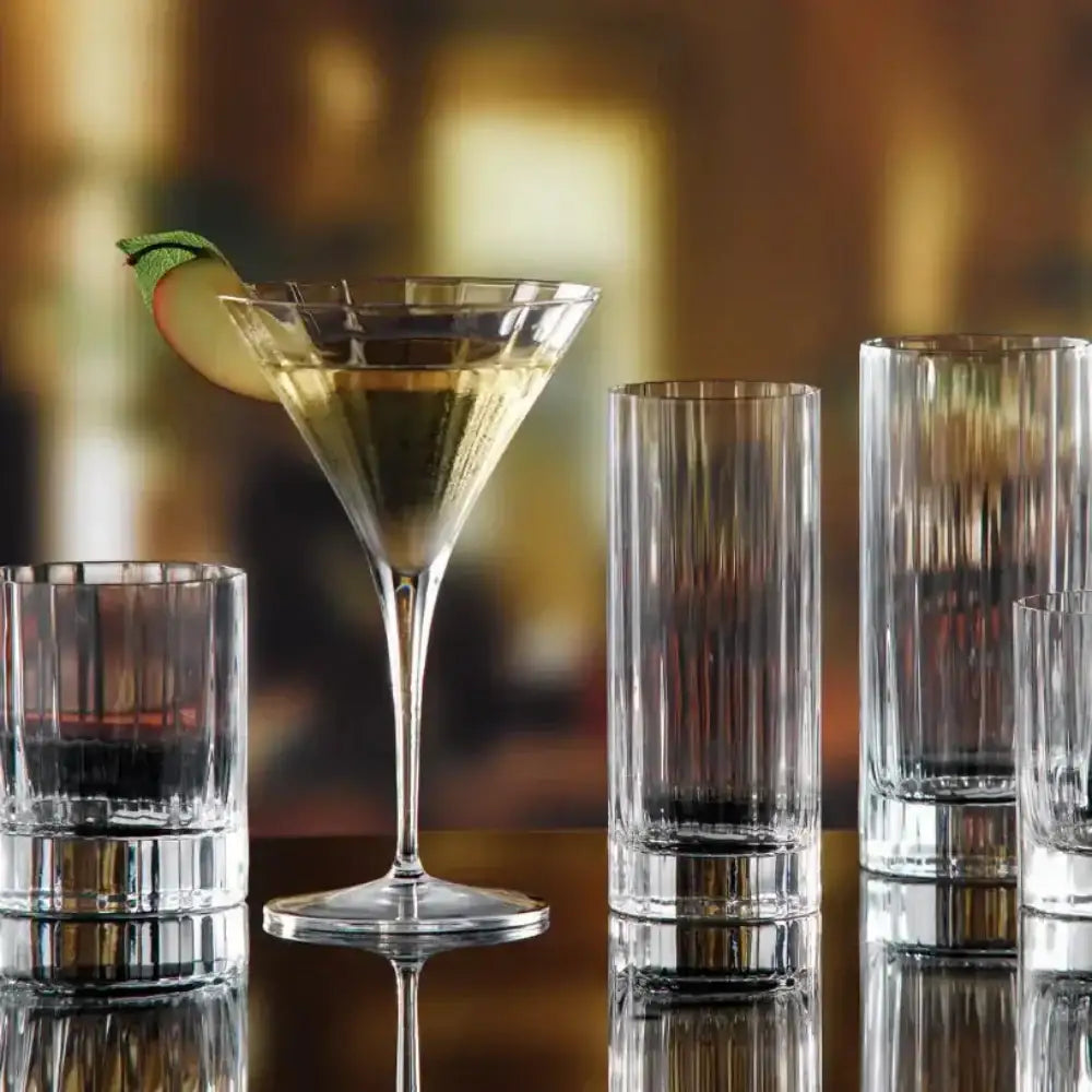 Cocktail with a lime garnish in a martini glass on a bar with other glasses.
