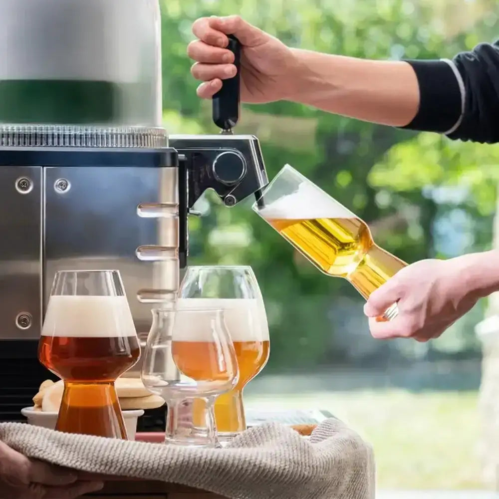 Person pouring beer from a tap into glasses with a blurred green outdoor background