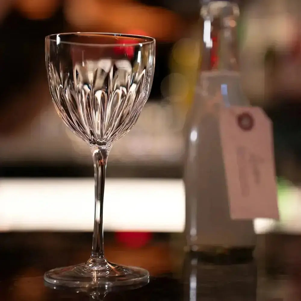 Clear glass wine glass on a bar counter with a blurred bottle in the background