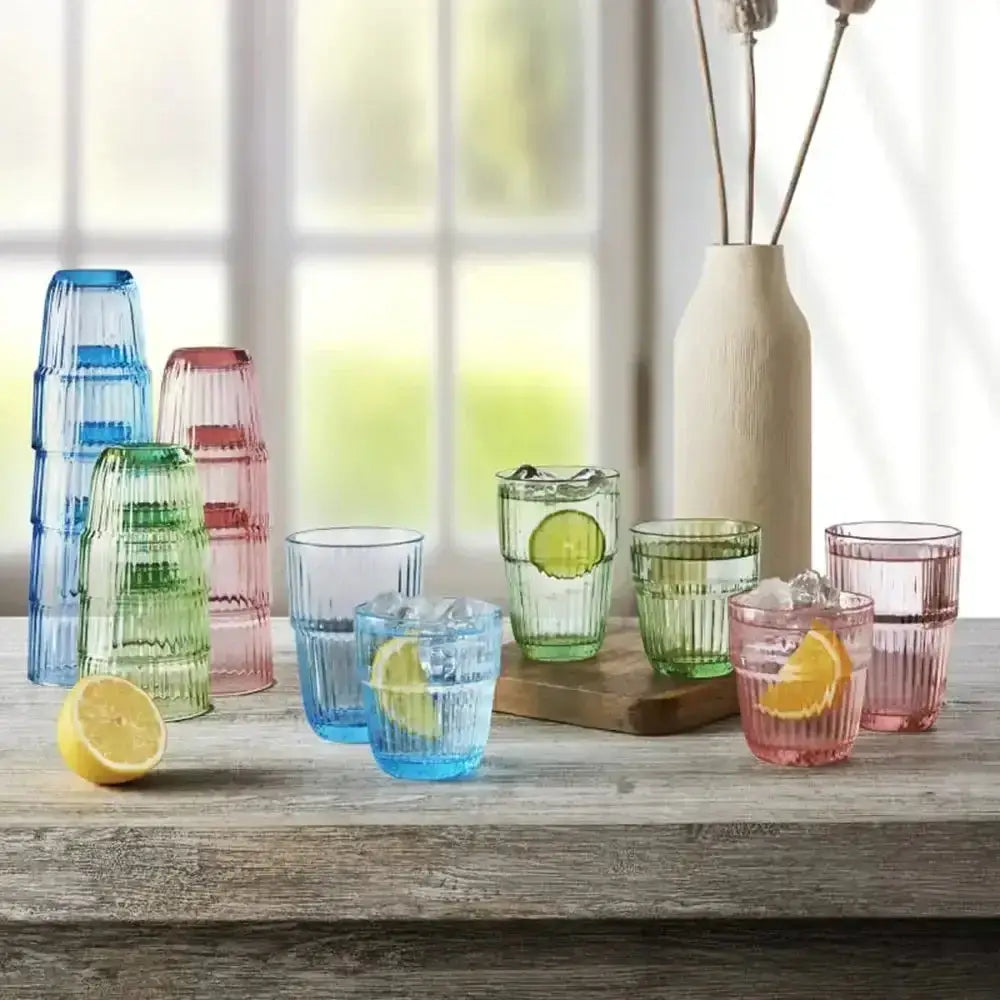 Colorful glass tumblers on a wooden surface with lemons and a vase in the background.