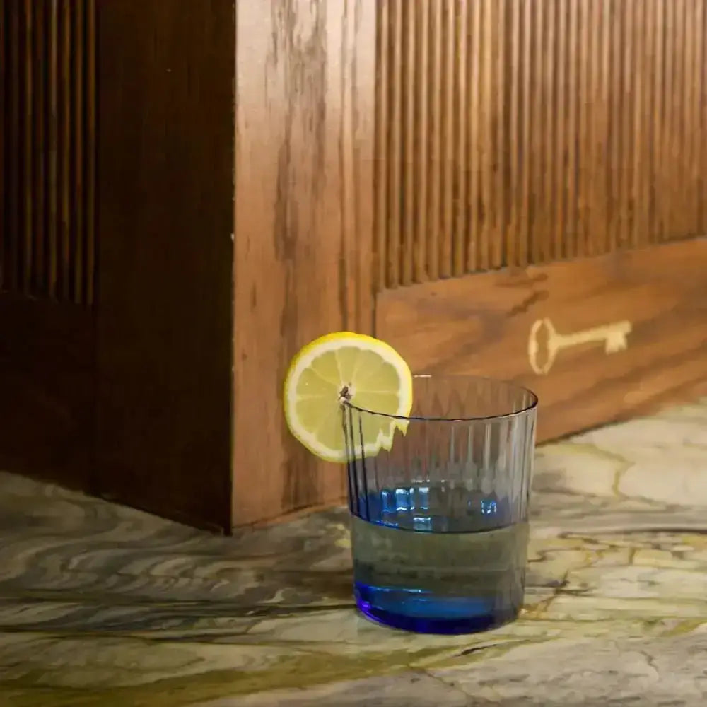 Blue glass with a lemon slice on a marble surface with wooden paneling in the background