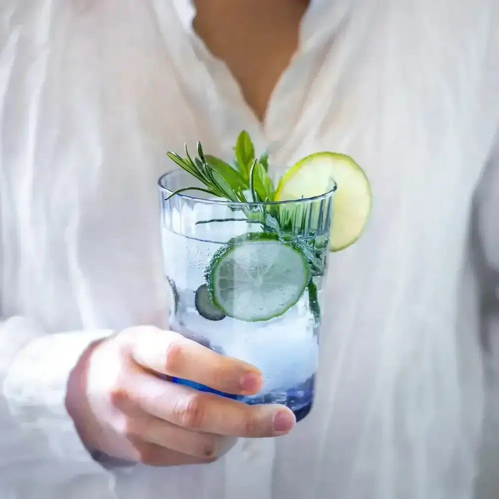 Person holding a glass of water with cucumber slices and mint leaves.