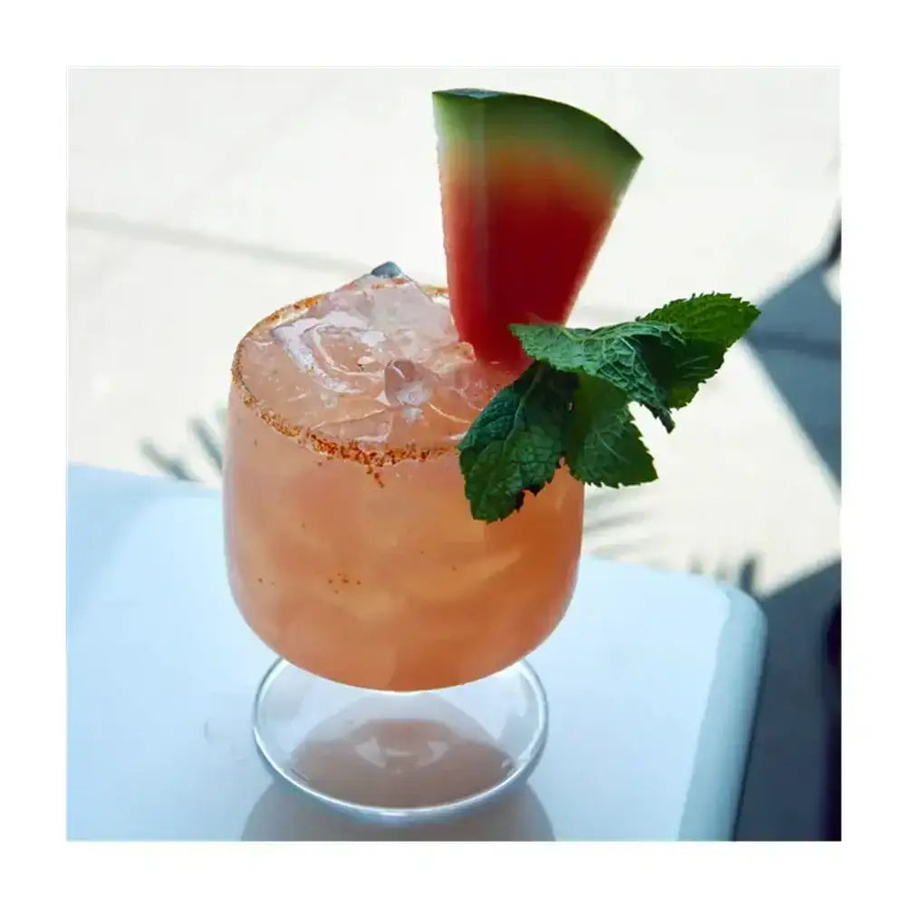 Cocktail with a slice of watermelon and mint leaf on a white surface